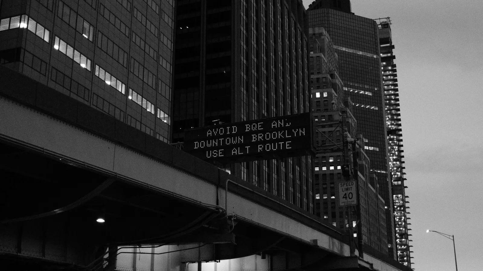 B/W photo of the 'S Street Viaduct' with a sign above saying 'Avoid BQE and Downtown Brooklyn. Use alternate route'.