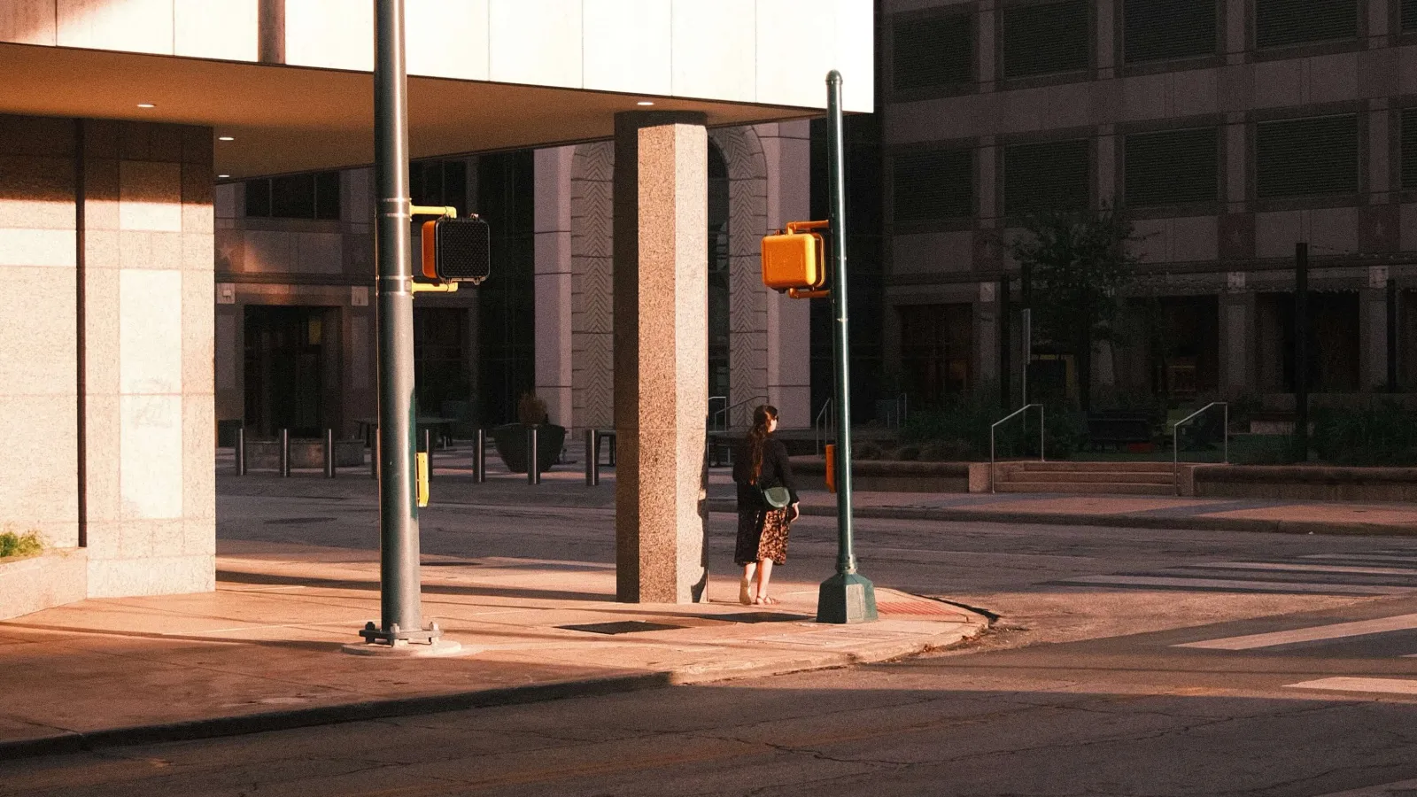 An intersection at Pecan Street in downtown San Antonio, with traffic lights and a person standing in early morning or late afternoon sunlight casting long shadows.