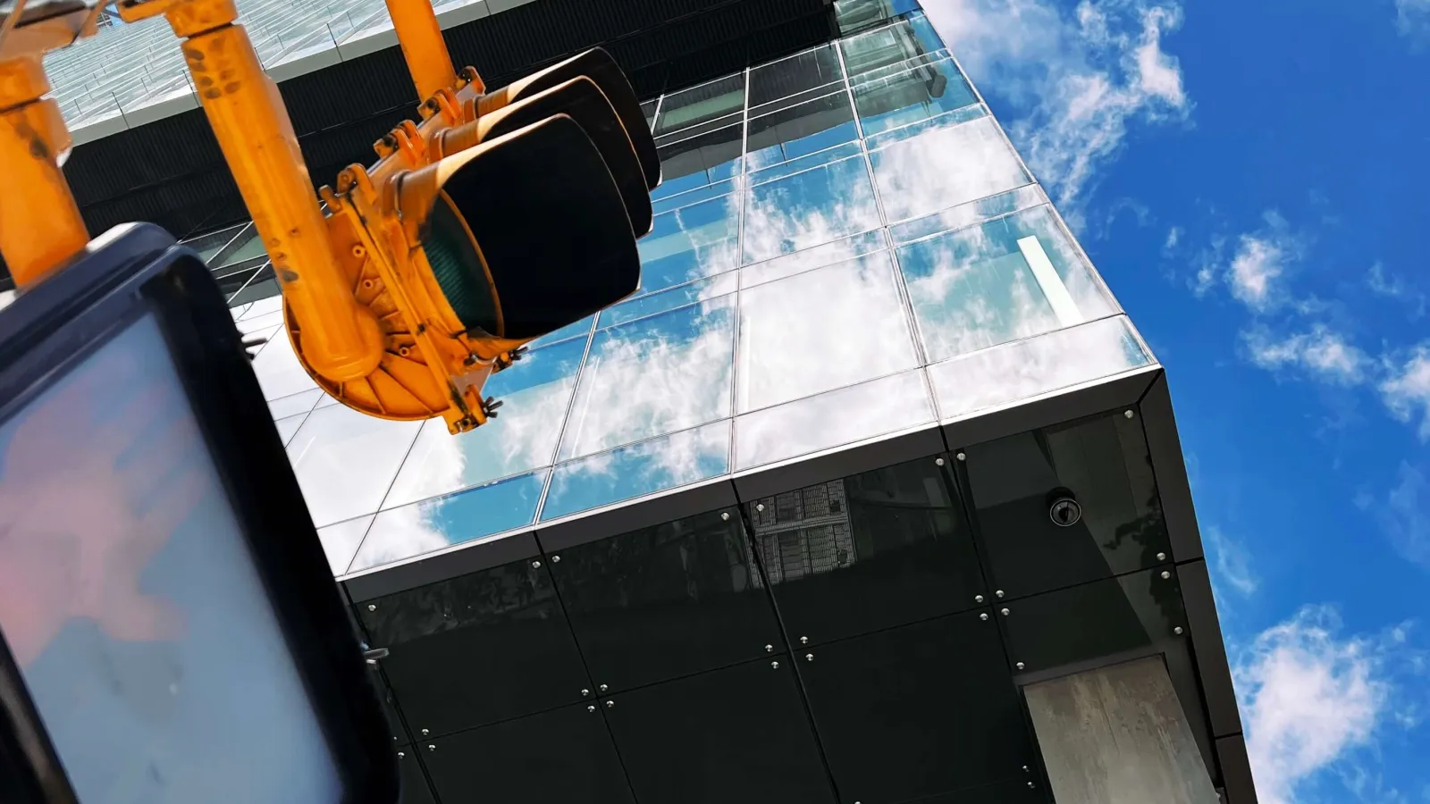 Close-up photo of a traffic light from the bottom looking up with a big building behind and the partly cloudy sky at the top.